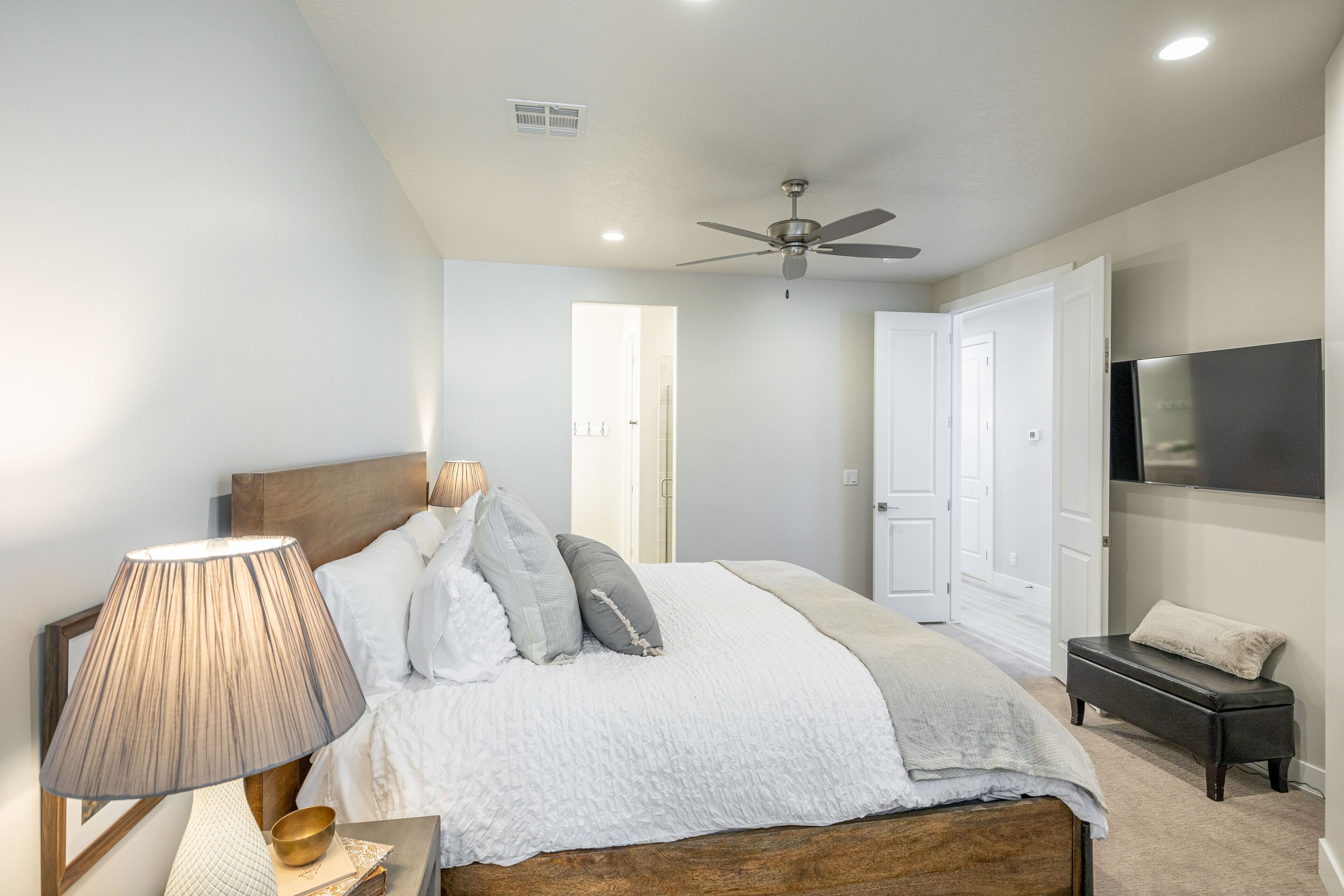 Un dormitorio con cama, lámpara de noche, ventilador de techo y televisión en la pared.