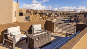 Eine Dachterrasse mit zwei Liegestühlen, einer Feuerstelle und Blick auf eine Wüstenlandschaft.