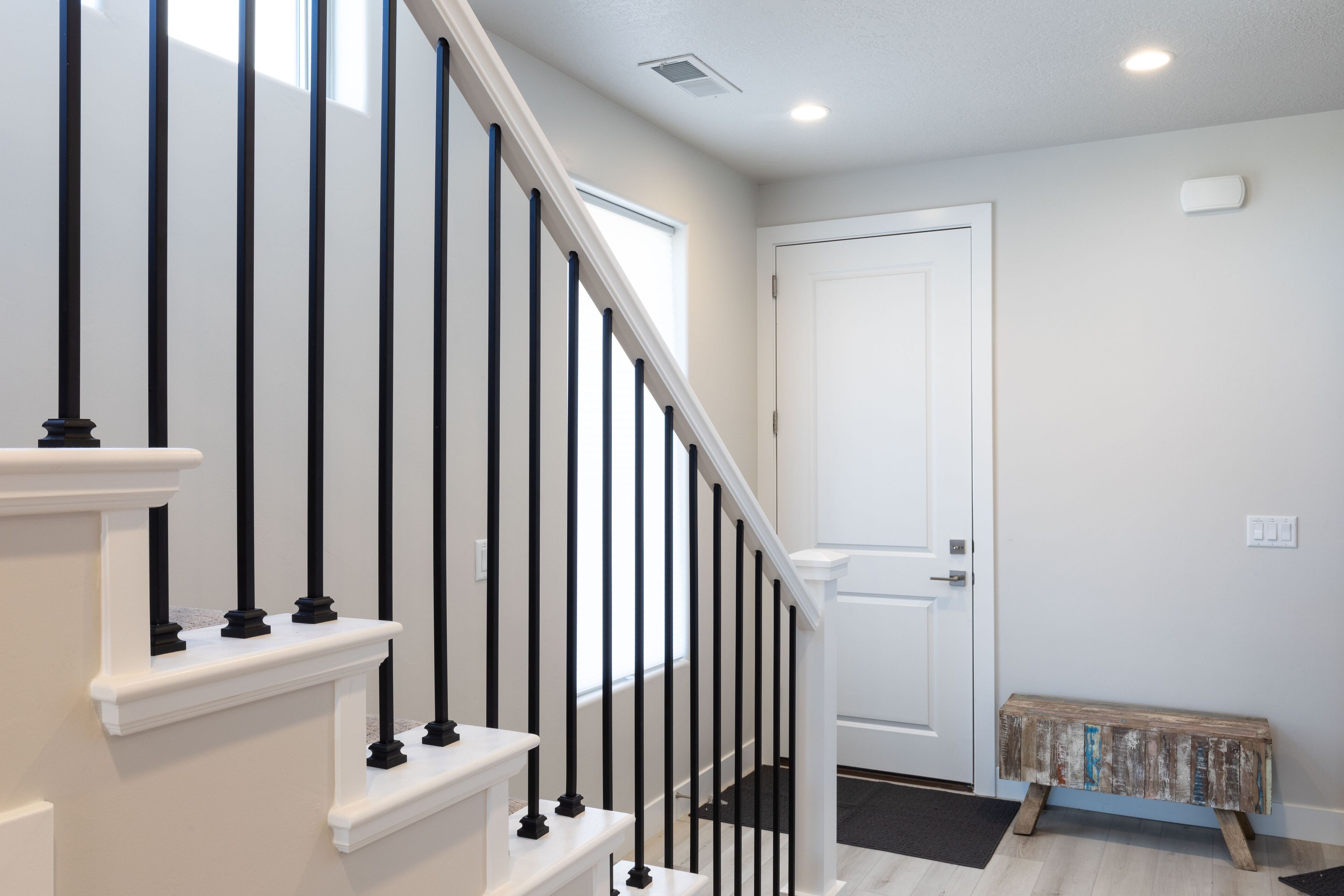 Un escalier avec des balustres noires et des rampes blanches, menant à une porte blanche.