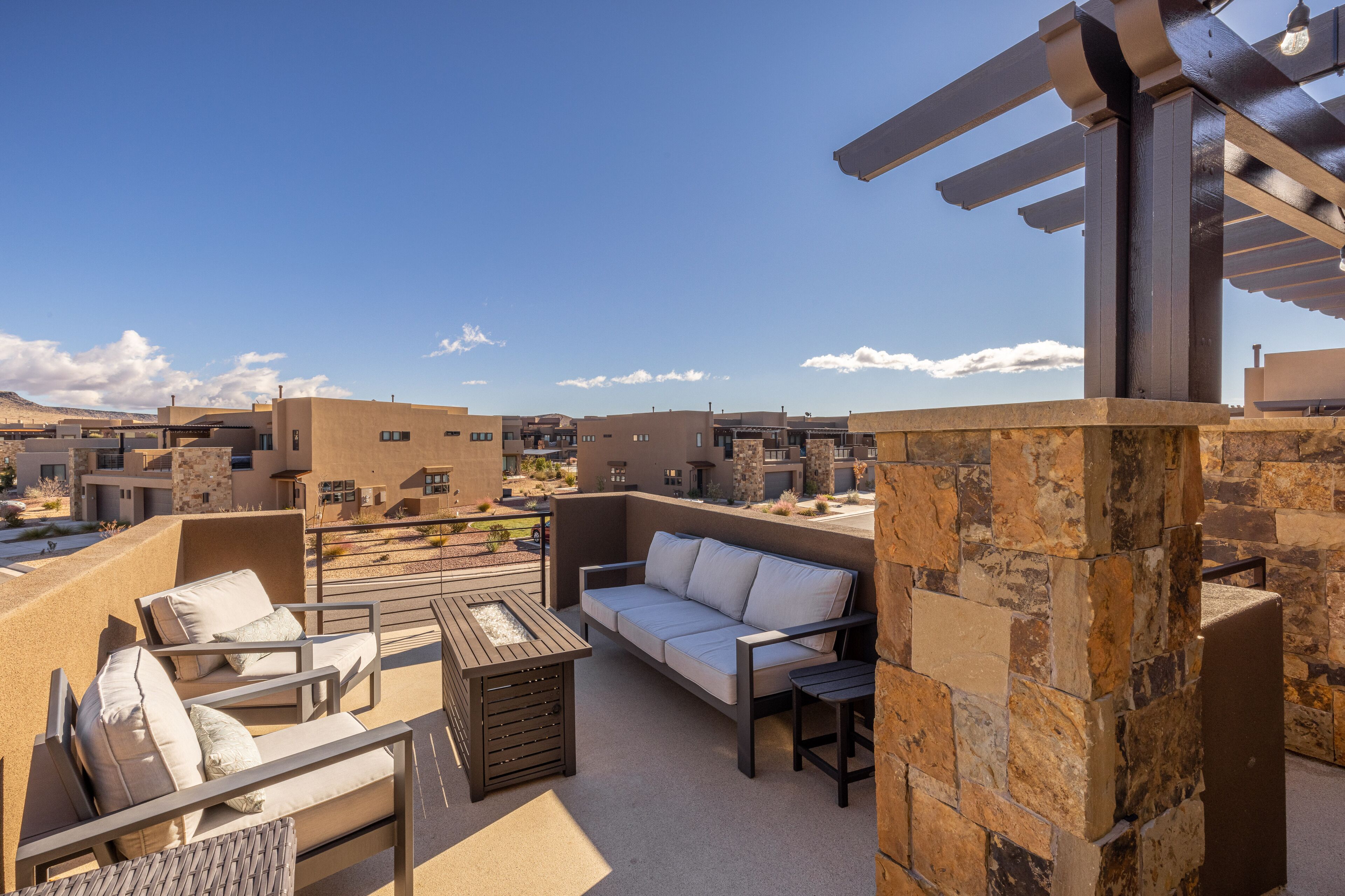 An outdoor patio with a sofa, chairs, and a table, surrounded by stone walls and a pergola.