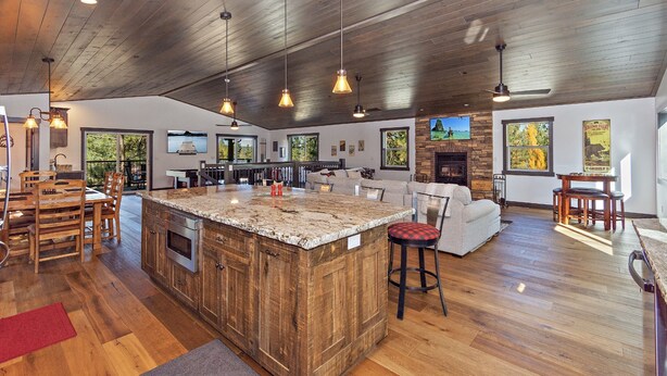 Un amplio salón con un gran techo de madera, una isla central con horno integrado y una chimenea de piedra.
