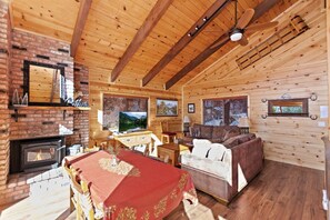 Interior de una cabaña de madera con chimenea, televisión y una zona de estar acogedora.