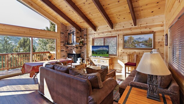 Een knus cabin interieur met houten plafond, een open haard, een televisie en een eethoek.