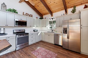 Una cocina moderna con armarios blancos, electrodomésticos de acero inoxidable y techo de madera.