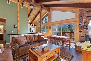 Interior acogedor de una cabaña con techo de madera, una zona de comedor con mesa y sillas, y una chimenea.