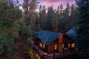 Une cabane dotée d’une terrasse et de nombreuses fenêtres, entourée d’une forêt dense.