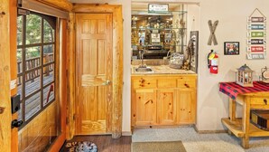Una puerta de madera con un ventanal, una pequeña cocina con un fregadero y armarios, y un letrero que dice "WISHIN' I WAS FISHIN'".