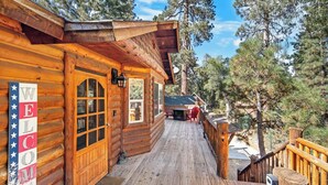 Una cabaña de madera con terraza, un cartel de bienvenida y vistas al bosque circundante.