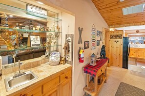 Cocina con mostrador de madera, pileta y varios utensilios de cocina. Hay un cartel en la pared y un extintor.