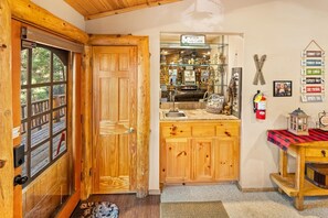 A wooden interior with a glass door leading to a balcony, a wooden cabinet with a sink, and a wall-mounted sign with various ski-related terms.