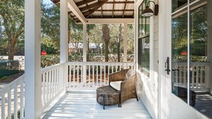 A covered porch with a wicker chair and a stop sign in the background. - 🐟Bikes-Walk 2 Beach-Calm Breeze Cottage (Santa Rosa Beach)