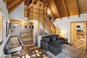A spacious living area with a wooden staircase, a foosball table, and a sofa.