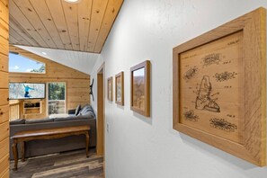 A wooden interior with a sofa, bench, and framed drawings on the wall. - Mooncrest Manor by Destination Big Bear : Expansive Mountain Views! Large Family Spaces! Pet Friendly! Game Room! (Big Bear Lake)