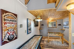 A room with a pool table, foosball table, and a dartboard. There are wall decorations including a sign for a pool bar and a vintage bowling sign. - Mooncrest Manor by Destination Big Bear : Expansive Mountain Views! Large Family Spaces! Pet Friendly! Game Room! (Big Bear Lake)