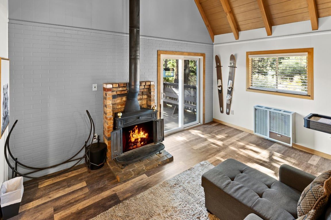 A cozy living room with a fireplace, wooden flooring, a sofa, and a ski rack.