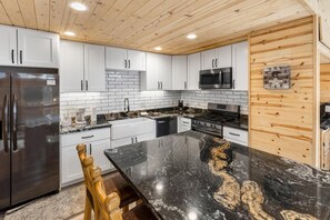 A modern kitchen with white cabinets, a black marble countertop, stainless steel appliances, and a wooden ceiling.