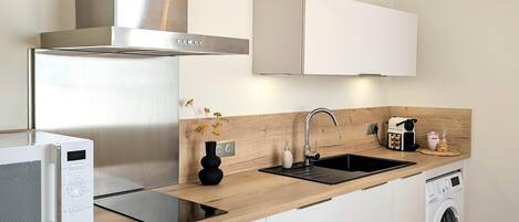 A modern kitchen with a stainless steel range hood, a built-in microwave, a sink with a faucet, a washing machine, and a wooden countertop.