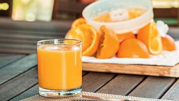 A glass of orange juice on a wooden table with a bowl of sliced oranges in the background.