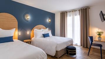 A hotel room with two beds, a desk, a chair, and a potted plant.