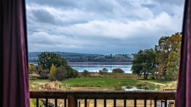 A balcony with a view of a lake, a car, and a building in the distance. - Drumlanrig Lodge with hot tub and views of Loch Lomond (Loch Lomond)