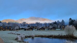 A row of log cabins with a clear path leading to a pond, surrounded by frosty trees and mountains in the background. - Drumlanrig Lodge with hot tub and views of Loch Lomond (Loch Lomond)