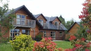 Eine Holzdiele mit Balkon, umgeben von üppigem Grün und einem gepflegten Rasen.