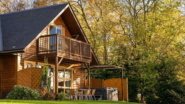 A wooden cabin with a balcony, a hot tub, and a grassy yard. - Cawdor  Diamond  Lodge with hot tub and Loch views (Balmaha)