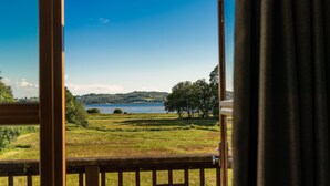 A view from a window overlooking a lake, grassy fields, and trees. - Cawdor  Diamond  Lodge with hot tub and Loch views (Balmaha)