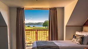 Habitación de hotel con cama, una silla y vistas a un lago y colinas.