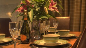 Una mesa de comedor dispuesta con platos, tazones y copas de vino, una botella de vino y un jarrón con flores.