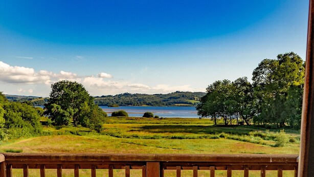 Un balcón con dos sillones de mimbre, una cama y vistas a un lago y colinas.