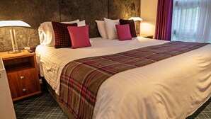 Een hotelkamer met een groot bed, twee nachtkastjes, een lamp en een raam met gordijnen.