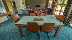 Een ruime woonkamer met een grote eettafel met glazen blad, omringd door houten stoelen, een comfortabele zithoek en een groot raam met gordijnen.
