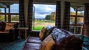 Ein Zimmer mit Ledersofa, einem kleinen Tisch und Blick auf ein grünes Feld durch große Fenster.