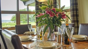 Ein Esstisch ist gedeckt mit Tellern, Besteck und Weingläsern, dazu eine Blumenvase und eine Champagnerflasche.