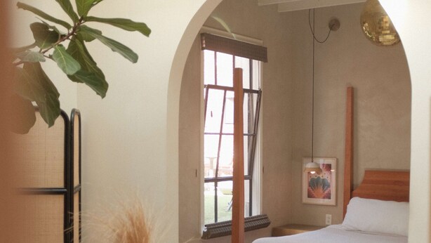 Ein Schlafzimmer mit großem Fenster, einem Bett, einem Nachttisch und einem Wandbild.