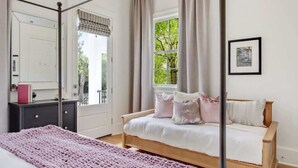 A bedroom with a four-poster bed, a bedside table, a dresser, and a window with curtains.