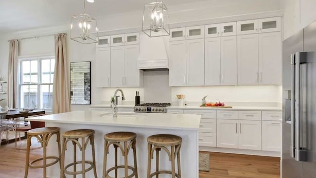 A modern kitchen with white cabinets, a central island with stools, a stainless steel refrigerator, and pendant lighting.