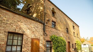 A brick building with a large window, a door, and a small window with a view of the sky. - Studio 3A, The Carriage House. (York)