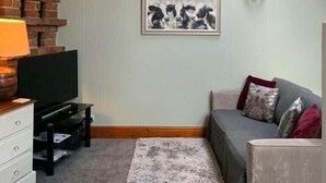 A cozy living room with a sloped ceiling, a fireplace, a flat-screen TV, a grey sofa, and a framed picture on the wall. - Studio 3A, The Carriage House. (York)
