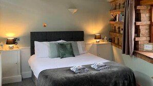 A bedroom with a bed, bedside tables, a headboard, a wall-mounted shelf, and a ceiling with exposed beams. - Studio 3A, The Carriage House. (York)
