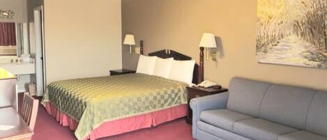 Quarto de hotel com cama, escrivaninha, poltrona, sofá e um quadro na parede.