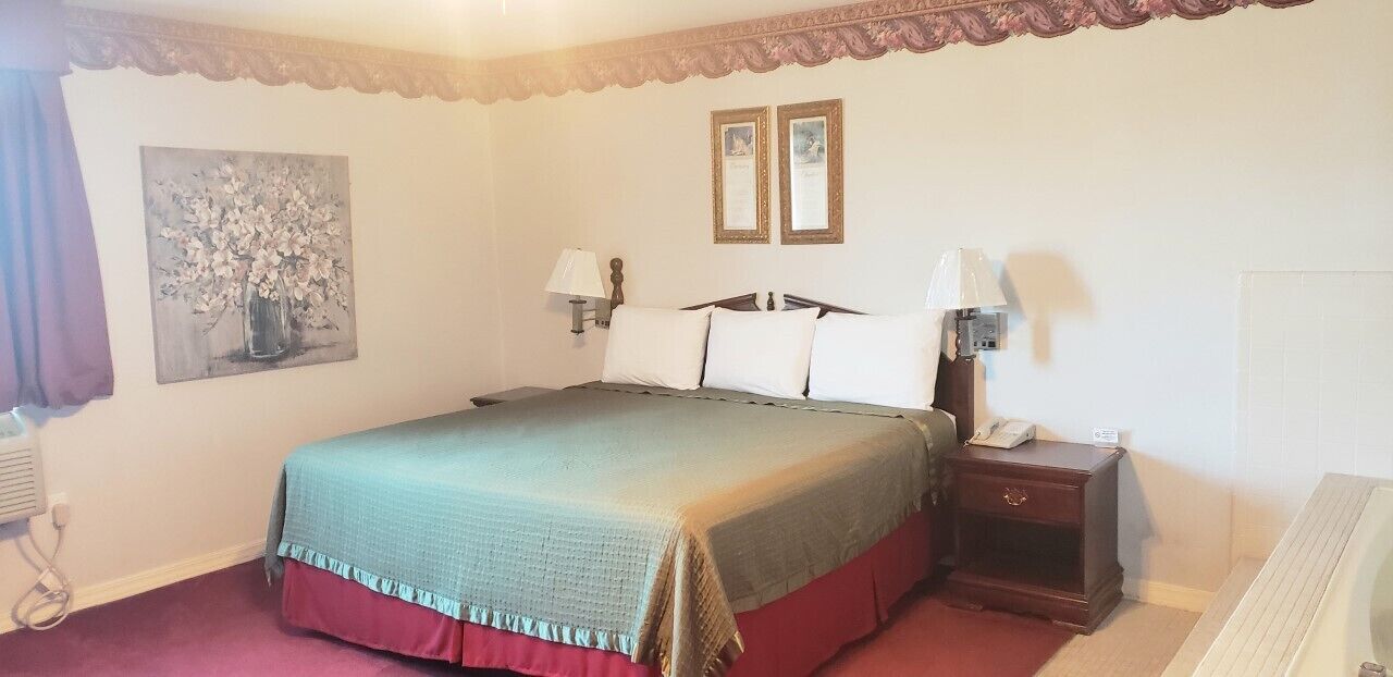 A hotel room with a bed, bedside lamps, a nightstand, a painting on the wall, and a window with curtains.