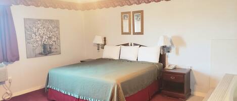 A hotel room with a bed, bedside lamps, a nightstand, a painting on the wall, and a window with curtains.