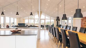 A spacious kitchen with a central island, a dining area with a long wooden table and chairs, and large windows allowing natural light. - Holiday Home in LÃ¦sÃ¸ (Læsø)