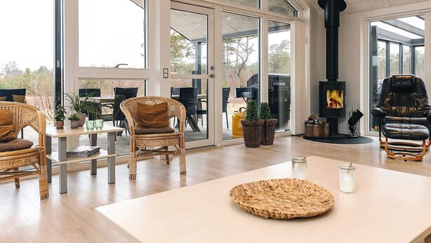 A spacious living area with large windows, a fireplace, wicker furniture, and a view of the outdoors. - Holiday Home in LÃ¦sÃ¸ (Læsø)