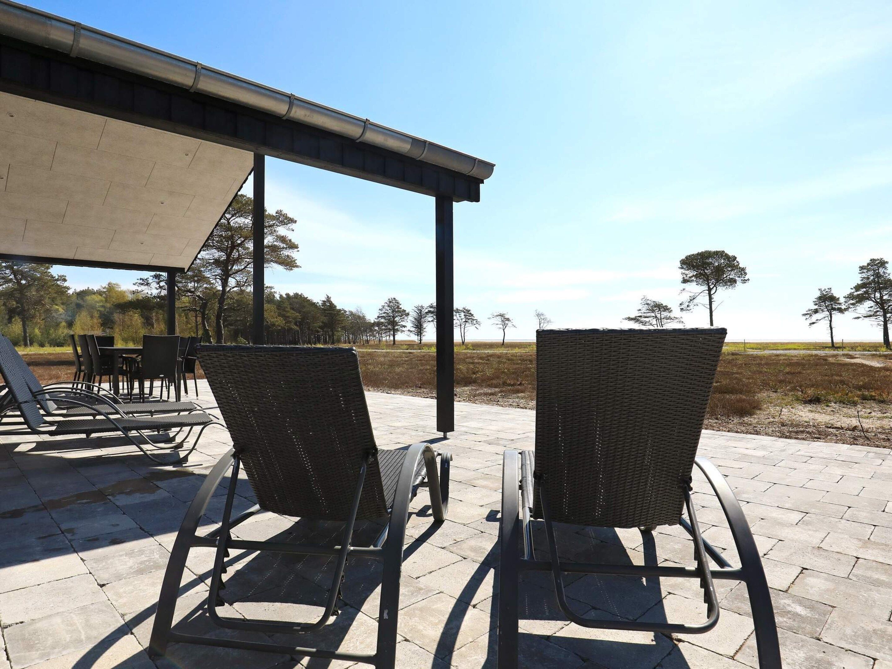 Buiten zitplaatsen met stoelen en tafels, een overdekt gedeelte en uitzicht op bomen en open land.