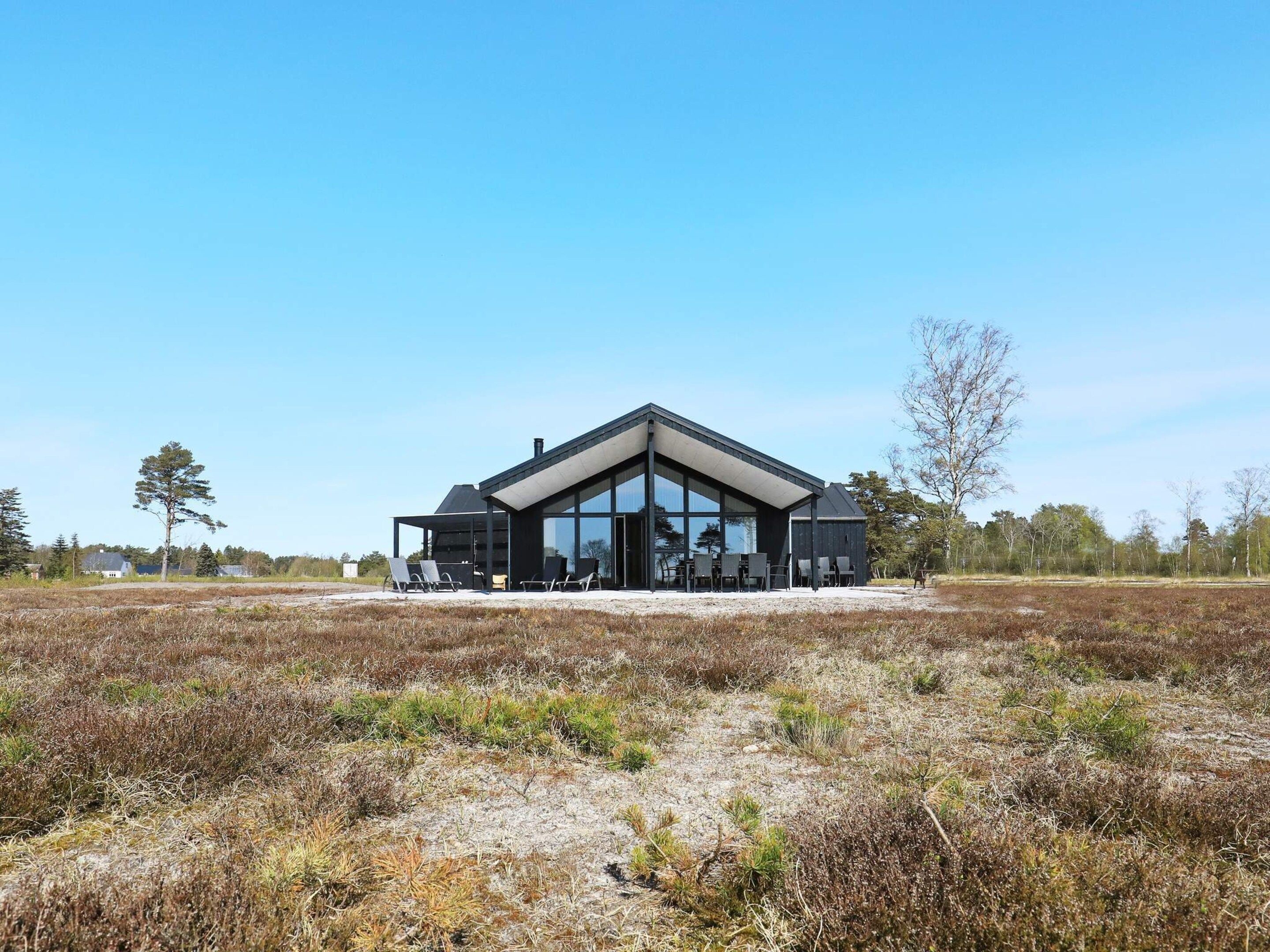 A modern building with large glass windows, a covered outdoor seating area, and a natural landscape surrounding it.