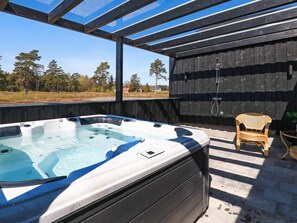 A hot tub with a wooden deck and a wicker chair, surrounded by a wooden fence and trees.
