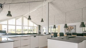 A modern kitchen with white cabinets, a large island, pendant lighting, and large windows. - Holiday Home in LÃ¦sÃ¸ (Læsø)